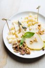 From above of square pieces of cheese with skewers decorated with fresh mint and slices of pear with walnut in restaurant — Stock Photo