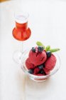 Сверху фиолетовые шарики мороженого в стеклянной чаше украшены свежей черникой и мятой и подаются со стаканом красного напитка в ресторане — стоковое фото