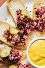 Draufsicht auf geröstete Brotscheiben mit buntem Salat und abgerundeten Salatgurkenstücken auf ovalem weißem Teller mit gelber Sauce — Stockfoto