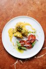 Vista dall'alto di pezzi di carne arrotondati in salsa gialla ed erbe aromatiche su piatto bianco con fette di menta di pomodoro e cipolla rossa nel ristorante — Foto stock