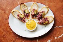 Вид зверху смажені скибочки хліба з барвистим салатом і округлими шматочками солоних огірків на овальній білій тарілці з жовтим соусом — стокове фото