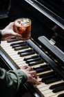 De cima de homem sem rosto tocando piano com um e e segurando vidro com coquetel i outra mão — Fotografia de Stock