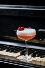 Red alcohol cocktail in stylish glass with white foam decorated with fresh raspberry on piano keys in restaurant — Stock Photo