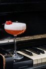 Cocktail di alcool rosso in vetro elegante con schiuma bianca decorata con lampone fresco sui tasti del pianoforte nel ristorante — Foto stock