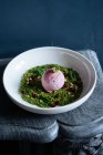 Сверху совок фиолетового мороженого на зеленом муссе, украшенном орехами и свежей мятой в белой миске — стоковое фото