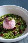 Сверху совок фиолетового мороженого на зеленом муссе, украшенном орехами и свежей мятой в белой миске — стоковое фото