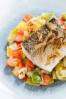 De arriba del filete el pez con los trozos pequeños cuadrados de los pimientos en el plato en el restaurante - foto de stock