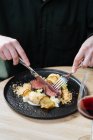 Cultivez d'en haut de la personne avec une assiette noire avec des tranches de rosbif sur une sauce crémeuse avec du chou-fleur et des frites en dînant avec un verre de vin rouge — Photo de stock
