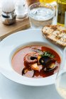 Вид зверху на червоний суп з восьминогів і мідій, поданий з зеленню і смаженим хлібом в ресторані — стокове фото