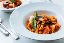 From above of tasty pasta with fresh pieces of tomato and eggplants decorated with basil leaves and sauce in restaurant — Stock Photo