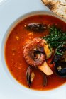 Blick von oben auf die rote Suppe aus Kraken und Miesmuscheln, serviert mit Grün und gebratenem Brot im Restaurant — Stockfoto