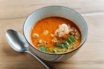 From above of spicy soup delicacy with shrimps and greenery in ceramic bowl on table with metal spoon — Stock Photo