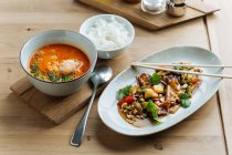 Draufsicht auf buntes Gemüse in ovalen Teller mit Essstäbchen auf Holztisch mit würzigen Meeresfrüchten Suppe und mit gekochtem Reis — Stockfoto