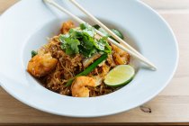 From above of tasty noodles with fried shrimps slices of lime and fresh parsley in plate with wooden chopsticks — Stock Photo