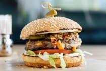 Primo piano di hamburger succoso con gustose fette di costoletta di lattuga di pomodori e cetrioli tra morbidi panini arrosto nel ristorante — Foto stock