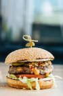 Closeup of juicy burger with tasty cutlet slices of tomatoes lettuce and cucumbers between soft roasted buns in restaurant — Stock Photo