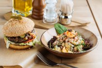 Big hamburger on paper with cutlet cheese and vegetables served with bowl of colorful salad in modern restaurant — Stock Photo