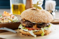 Hambúrguer grande em papel com queijo de costeleta e legumes servidos com tigela de salada colorida no restaurante moderno — Fotografia de Stock