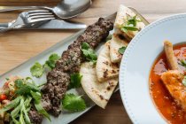 Draufsicht auf rote Suppe mit Fleisch und frischen Kräutern auf Holztisch mit Dönerspieß und Fladenbrot im Restaurant — Stockfoto