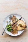 Вид на вкусные жареные куски мяса на белой тарелке с жареным хлебом, украшенным зеленым соусом и металлической вилкой в ресторане — стоковое фото