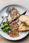 Blick von oben auf leckere gebratene Fleischstücke auf weißem Teller mit gebratenem Brot dekoriert mit Sauce Grün und Metallgabel im Restaurant — Stockfoto