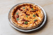Desde arriba de jugosa pizza al horno servida con queso, hierbas y tomate seco en la mesa en el restaurante - foto de stock