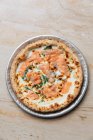 Top view of fresh baked pizza with cheese and slices of red fish decorated with herbs in restaurant — Stock Photo