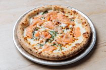 Blick von oben auf frisch gebackene Pizza mit Käse und Scheiben rotem Fisch mit Kräutern im Restaurant dekoriert — Stockfoto
