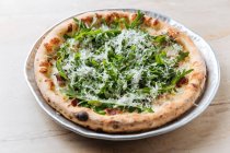 Closeup from above of tasty baked pizza decorated with green arugula and grated cheese in restaurant — Stock Photo
