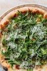 Крупный план сверху вкусной выпечки пиццы, украшенной зеленой рукколой и тертым сыром в ресторане — стоковое фото