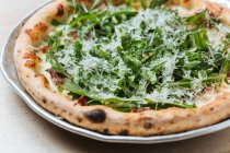 Primo piano dall'alto di gustosa pizza al forno decorata con rucola verde e formaggio grattugiato nel ristorante — Foto stock