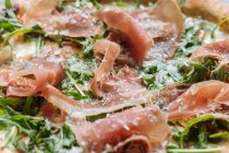 Blick von oben auf leckere Pizza mit dünnen Speckscheiben und frischem Grün auf dem Teller im Restaurant — Stockfoto