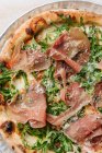 Top view of tasty pizza with thin slices of bacon and fresh greenery on plate in restaurant — Stock Photo