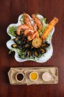 D'en haut de délicieuses crevettes grillées et moules aux légumes verts servis sur assiette blanche avec trois sauces sur le côté — Photo de stock