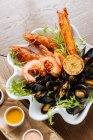 De cima de deliciosos camarões grelhados e mexilhões com verduras servidas em prato branco com três molhos na lateral — Fotografia de Stock