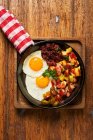 Top view of fried eggs with pieces of meat and vegetables in pan on wooden table — Stock Photo