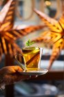 Crop hand with hot cocktail in glass decorated with slice of lemon anise and cinnamon — Stock Photo