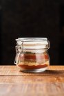 Lined with layers colorful spices in glass jar on wooden table isolated on black background — Stock Photo