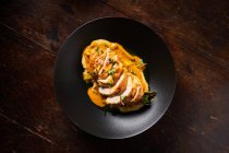 Vista dall'alto del filetto di pollo affettato al forno con salsa d'arancia colorata ed erbe verdi in elegante ciotola nera sul tavolo di legno — Foto stock