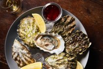 Top view of oysters on plate with ice and slices of lemons served with red sauce on wooden table in restaurant — Stock Photo