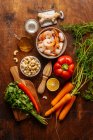 Top view of various ripe vegetables and herbs placed near juicer and boiled shrimps on wooden table in kitchen — Stock Photo