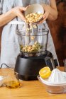 Donna irriconoscibile aggiungendo anacardi nel frullatore moderno mentre si prepara piatto sano in cucina — Foto stock