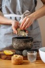 Donna irriconoscibile in grembiule macinare zenzero fresco in malta mentre si prepara piatto sano in cucina a casa — Foto stock