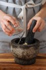Persona irreconocible en delantal derramando una taza de agua en el mortero mientras prepara salsa en casa - foto de stock