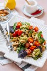 Apetitiva ensalada fresca sana y colorida con verduras y anacardos adornados con hojas de albahaca servidas en plato blanco con tenedores - foto de stock