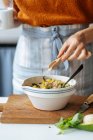 Кукурудзяна самиця з вимірювальною ложкою додаючи сіль в білу керамічну миску зі змішаними інгредієнтами під час приготування їжі на кухні — стокове фото