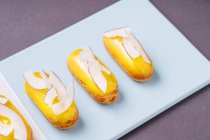 Primi piani gustosi eclairs con glassa di banana e pezzi di cocco posizionati su tavola blu — Foto stock