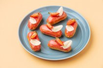 From above delicious eclairs with strawberry icing and white chocolate leaves placed on beige background — Stock Photo