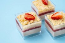 Nahaufnahme quadratische Glasbecher mit leckerem Erdbeermousse auf blauem Hintergrund — Stockfoto