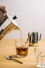 Erntehelfer gießt Kaffee aus Kaffeemaschine in stilvolles Glas mit Eis auf Holztheke im Café — Stockfoto